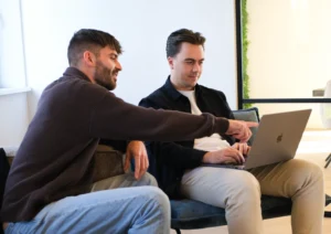 Twee mannen concentreren zich op een laptop in een moderne, lichte kantoorruimte.