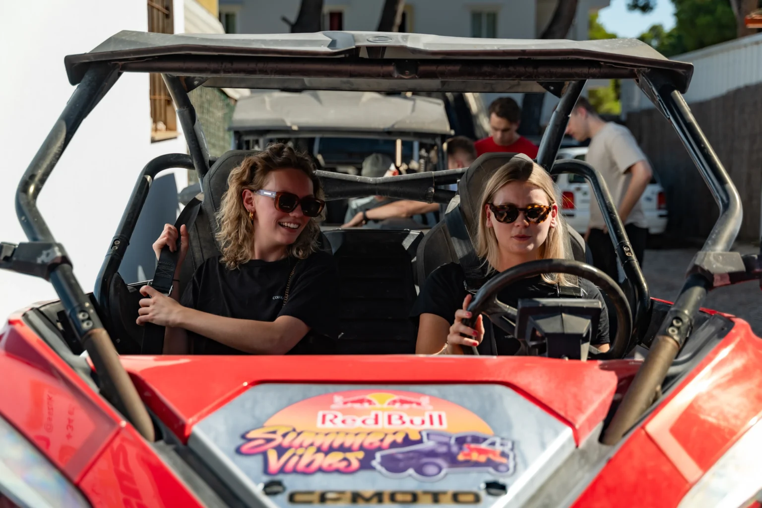 Twee vrouwen in een buggy met zonnebrillen en zwarte shirts, de buggy toont Red Bull Summer Vibes logo.