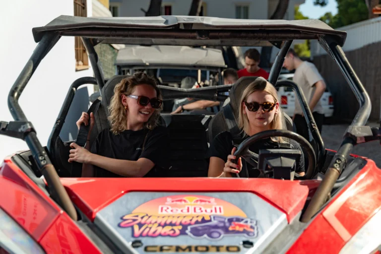 Twee vrouwen in een buggy met zonnebrillen en zwarte shirts, de buggy toont Red Bull Summer Vibes logo.