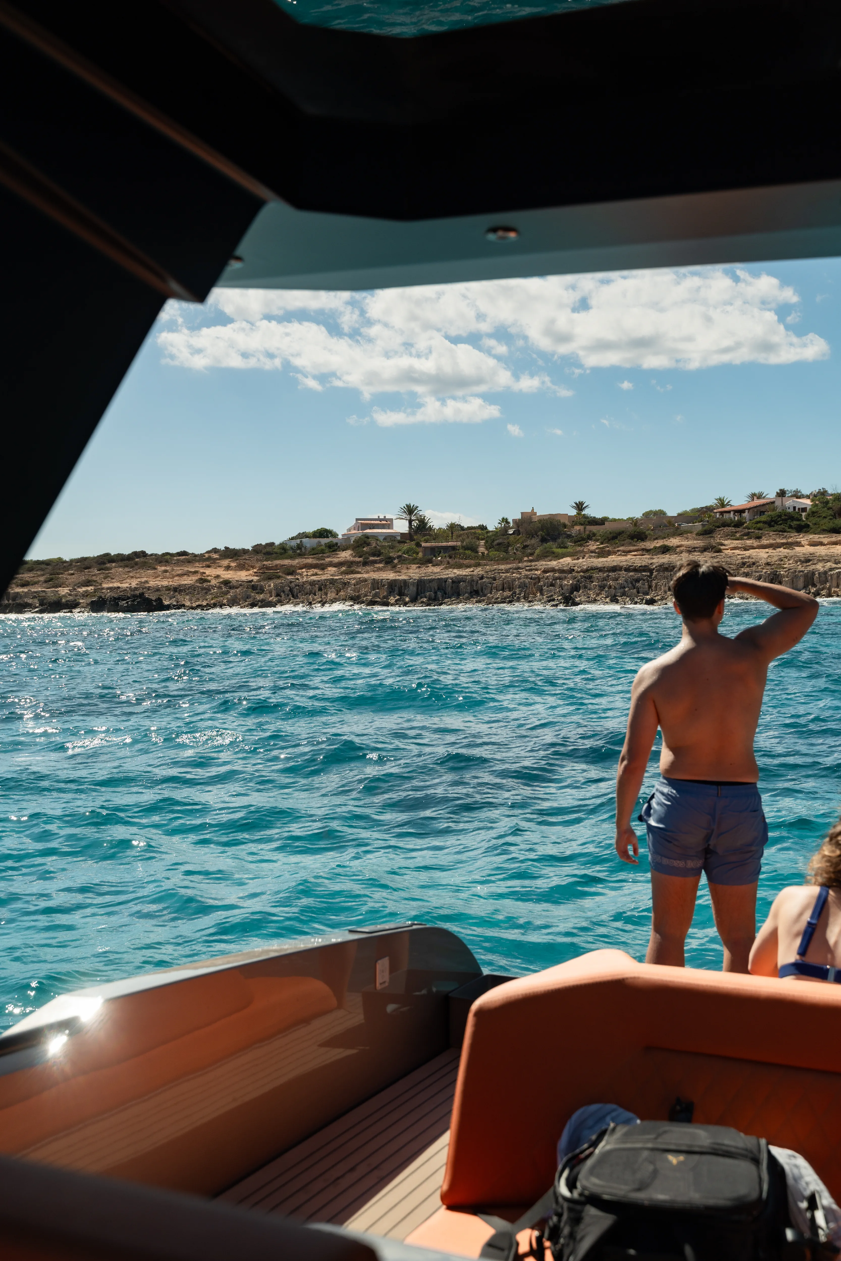 Man en vrouw op een boot met helderblauwe zee, kustlijn met huizen en palmbomen op zonrijke dag