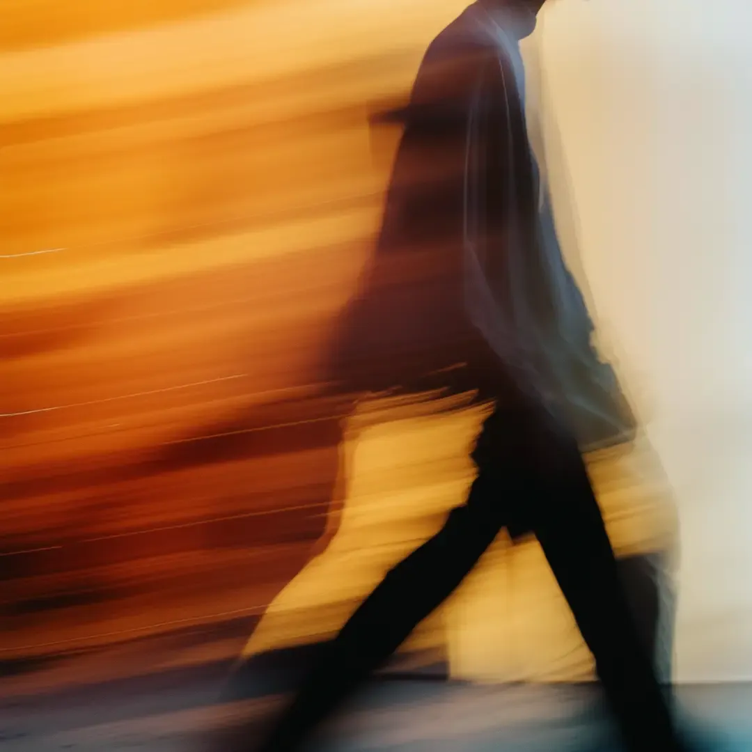 Persoon in beweging met lange sluitertijd gefotografeerd, zichtbaar als een vaag silhouet tegen warme oranje en gele achtergrond