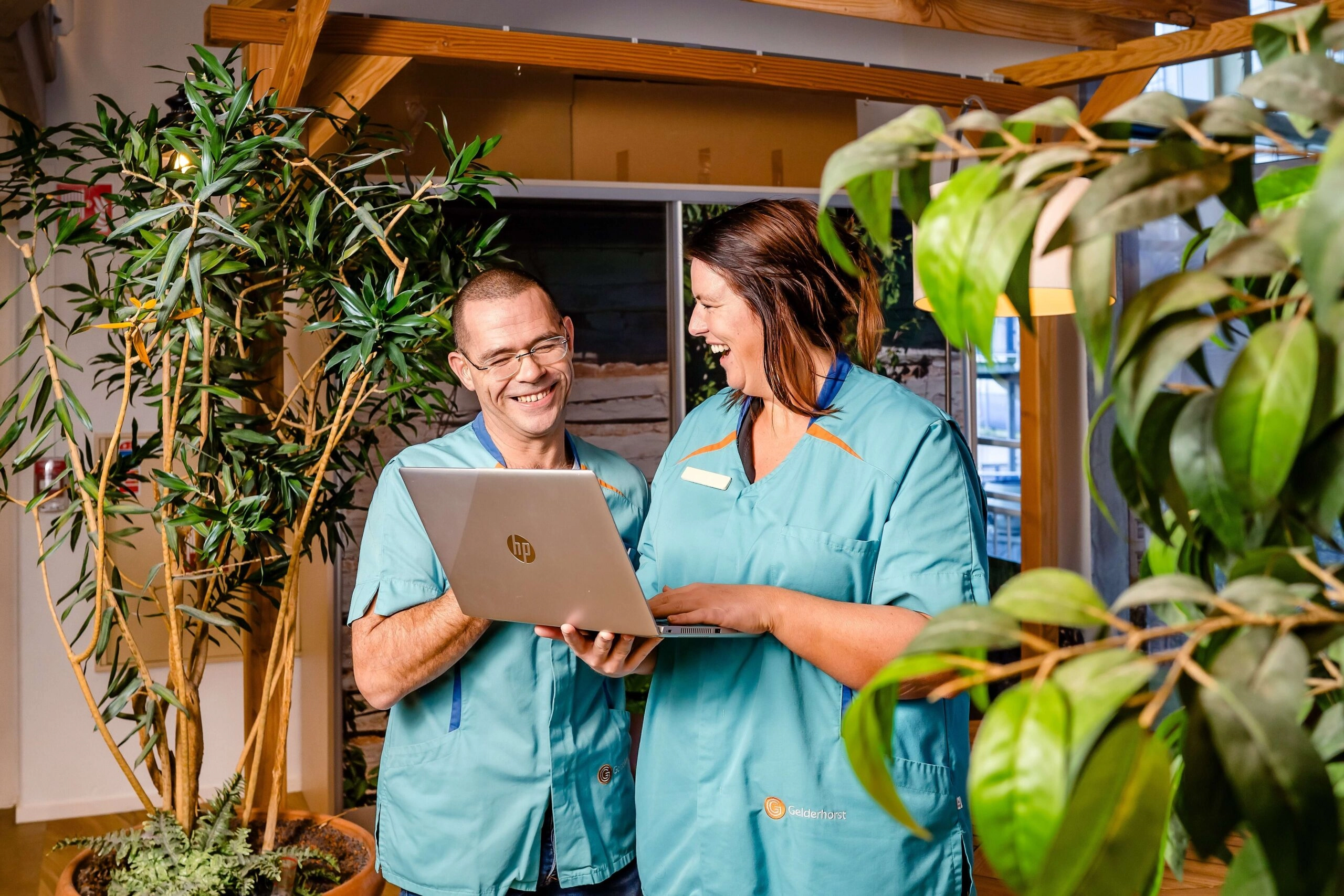 Twee zorgprofessionals in lichtblauwe uniformen met laptop in een groene, natuurlijke ruimte