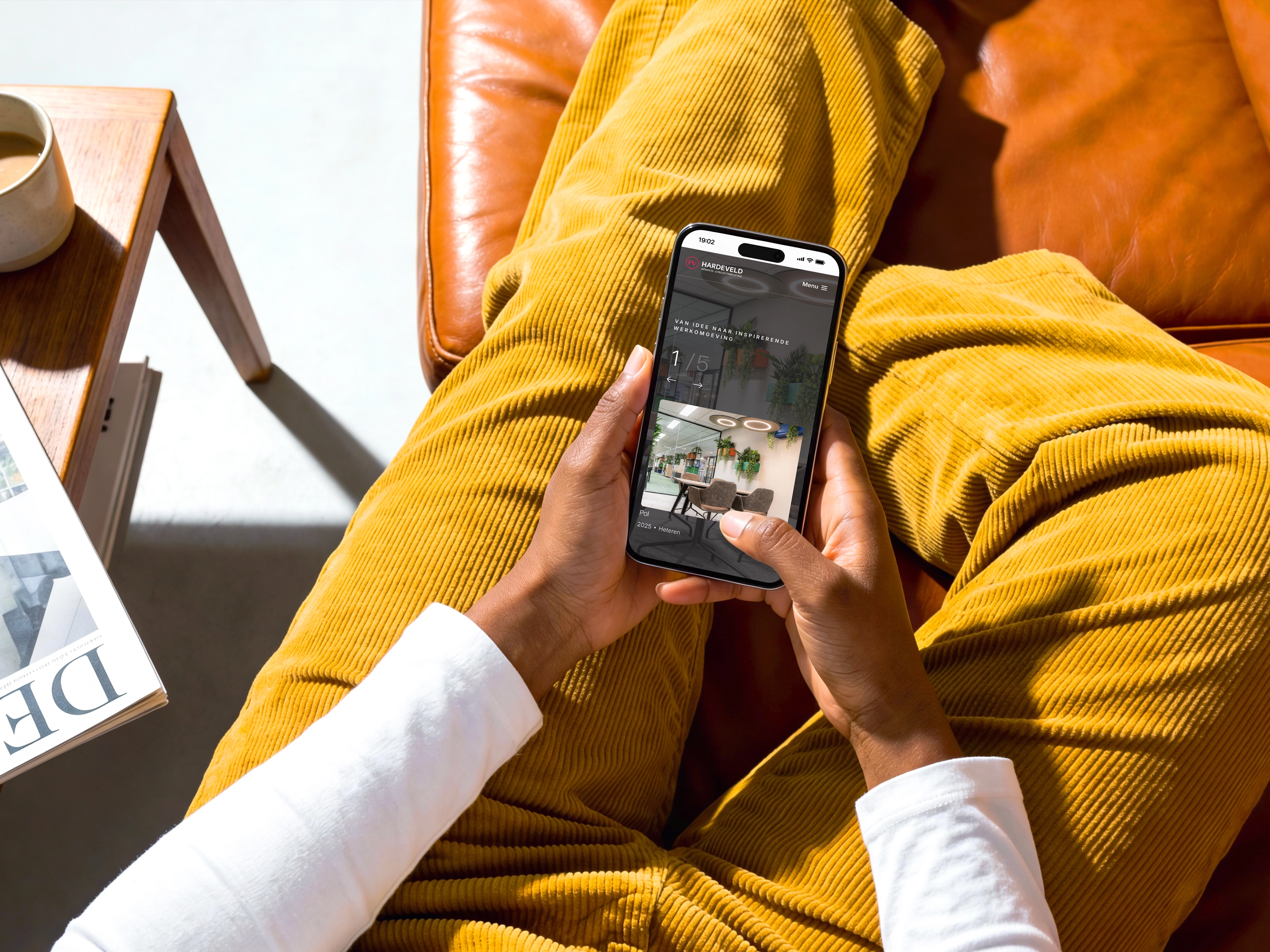 Persoon zit ontspannen op een leren bank met gekruiste benen en houdt een smartphone vast