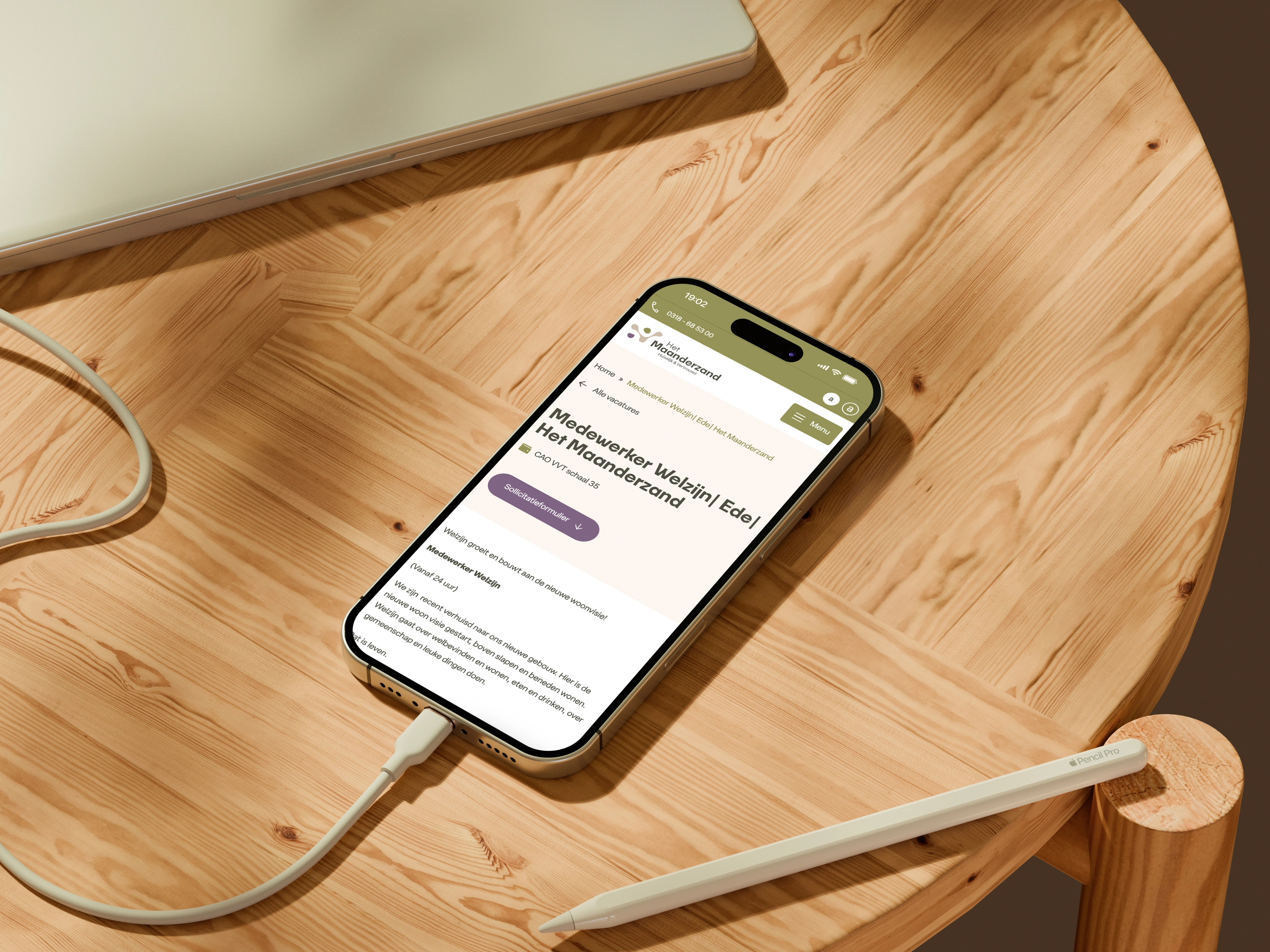 Houten tafel met smartphone die webpagina toont en stylus ernaast, deels opgeladen via kabel