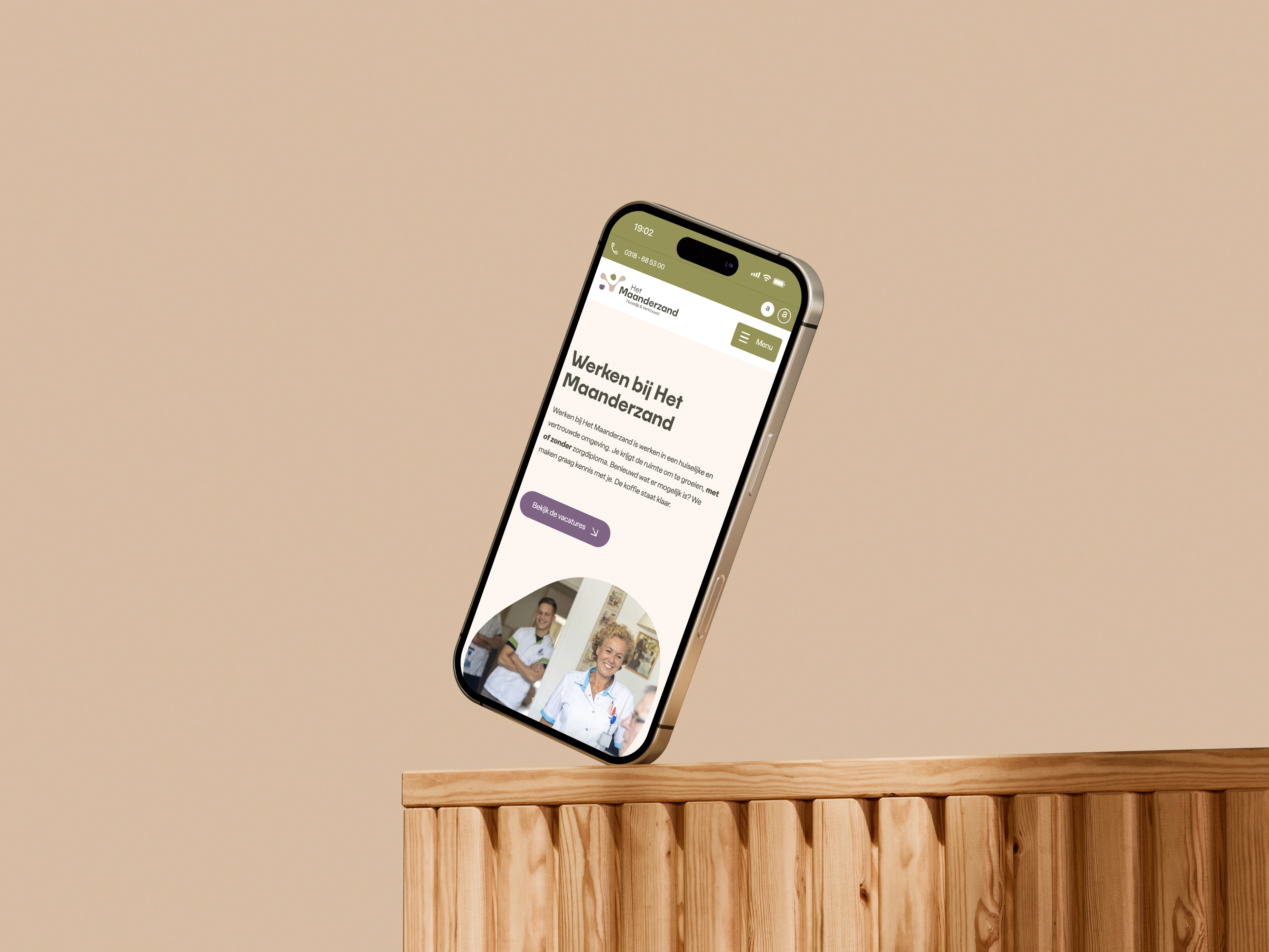 Smartphone met website 'Werken bij Het Maanderzand' op een houten oppervlak, beige achtergrond