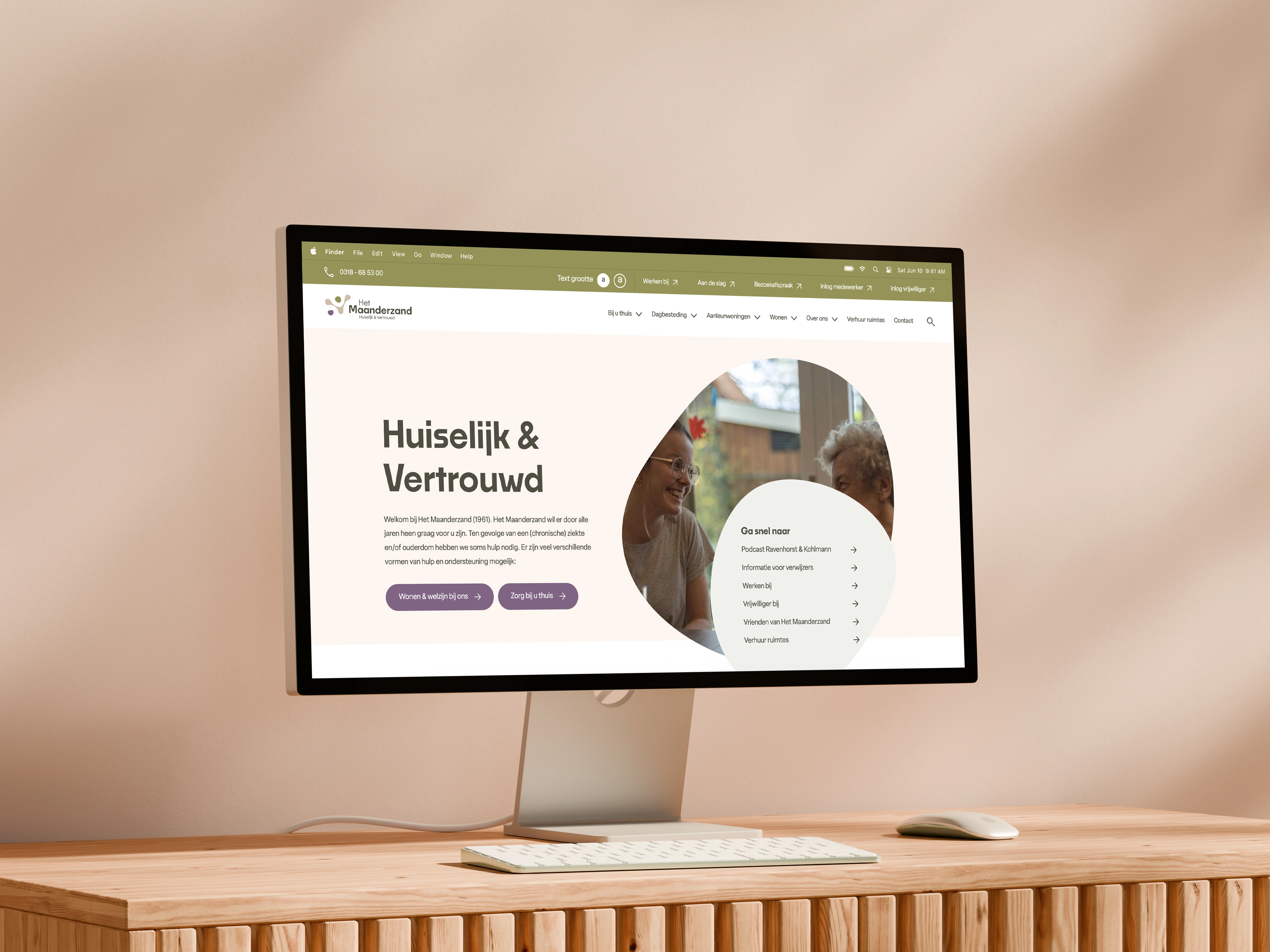 Computer op houten bureau toont website van Het Maanderzond met welkomsboodschap en interactieve secties