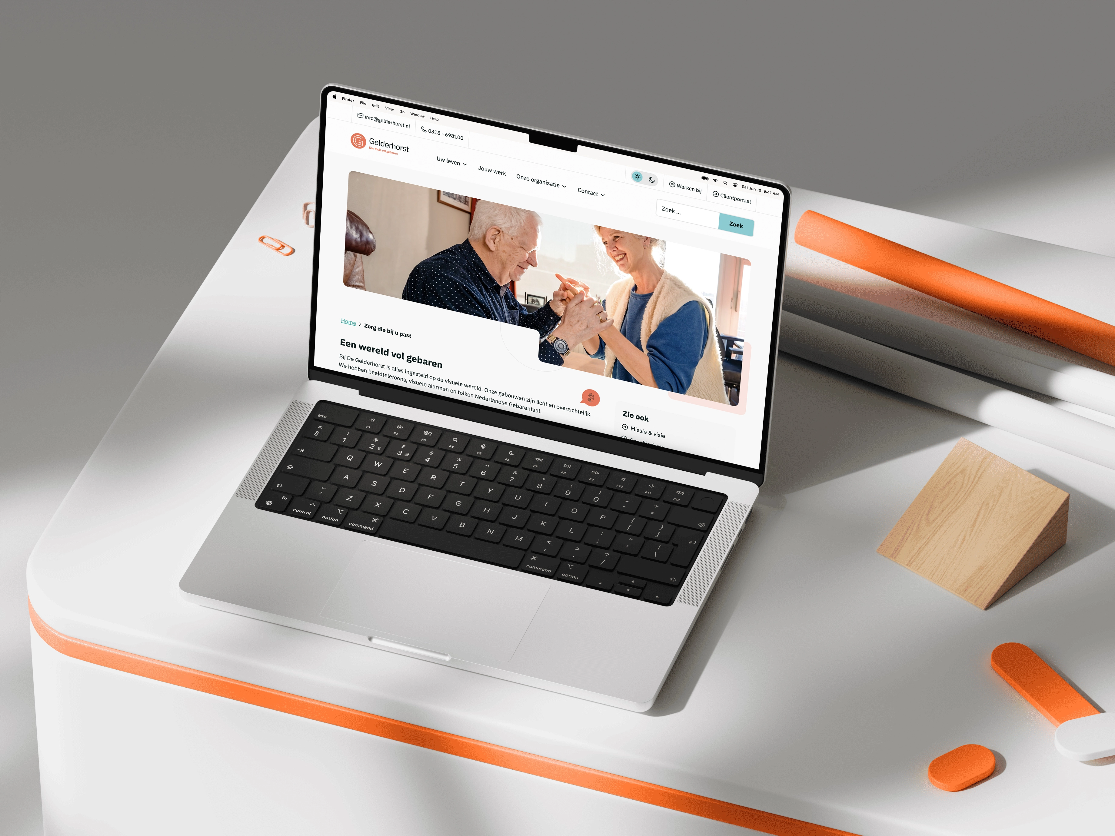 Moderne laptop op witte tafel met oranje rand toont website met kleurrijke visuals en accessoires op achtergrond