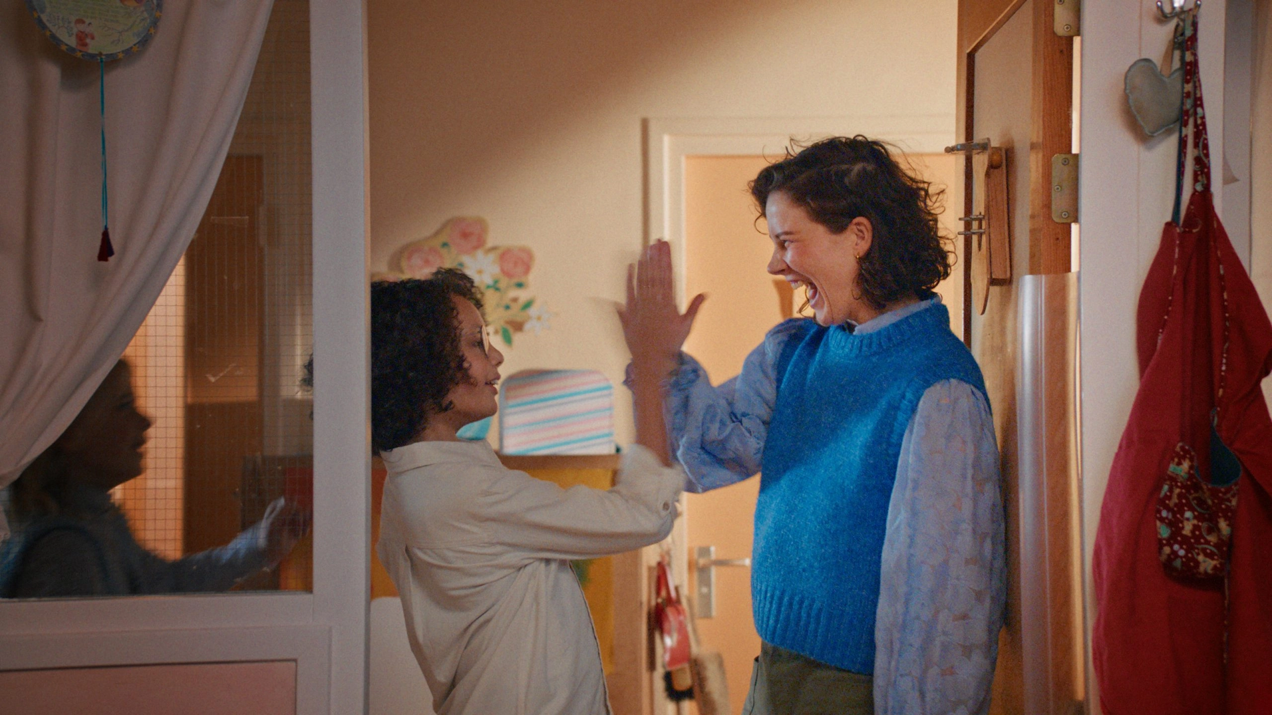 Twee mensen in huiselijke ruimte geven elkaar een high-five, achtergrond met deur en kast